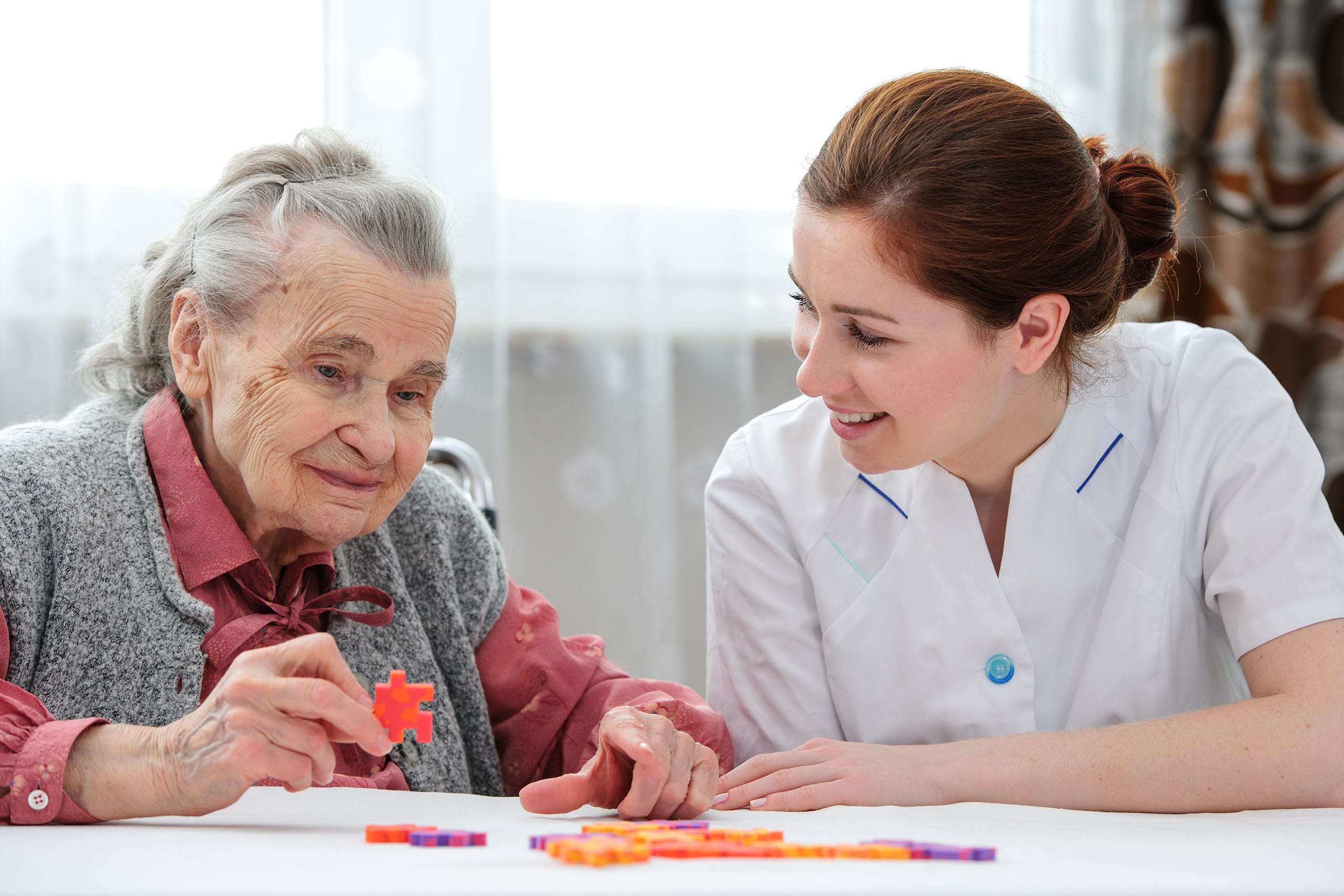 Care giver helping senior woman with a memory care activity.