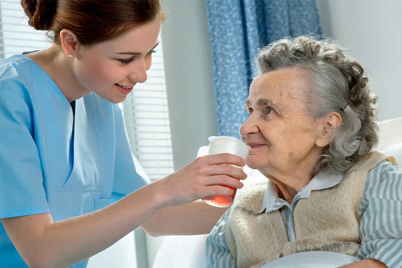 Caregiver helping senior woman to drink.