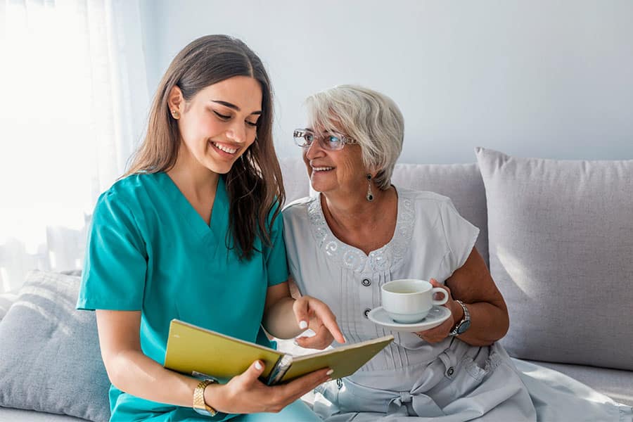 Caregiver with her patient sitting on the sofa concept image for routine home care.