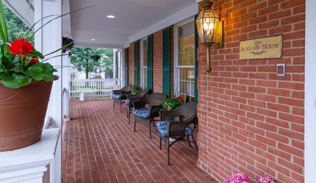 Front porch of The Auxiliary House, a welcoming and peaceful memory care home with seating and flowers Front porch of The Auxiliary House, a welcoming and peaceful memory care home with seating and flowers