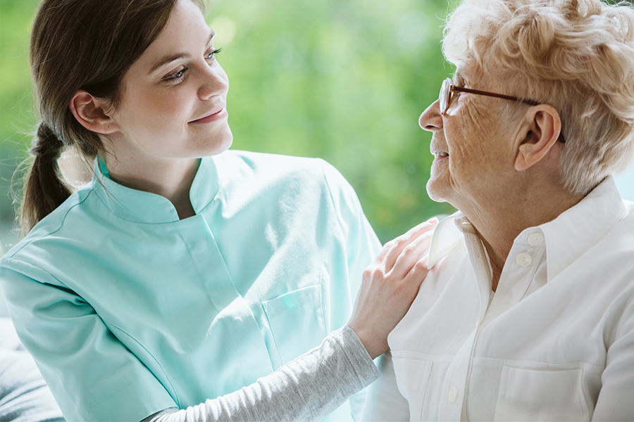 Caregiver providing tailored personal care services, smiling and supporting an elderly woman with a hand on her shoulder.