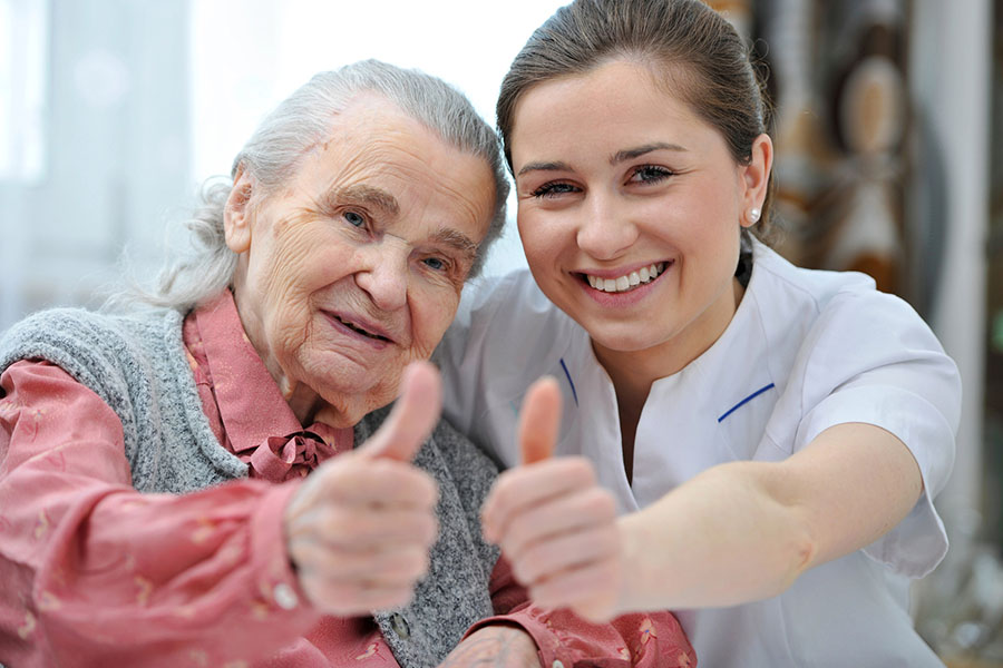 Elderly woman and hospice caregivers smiling together and giving thumbs-up, symbolizing positive care