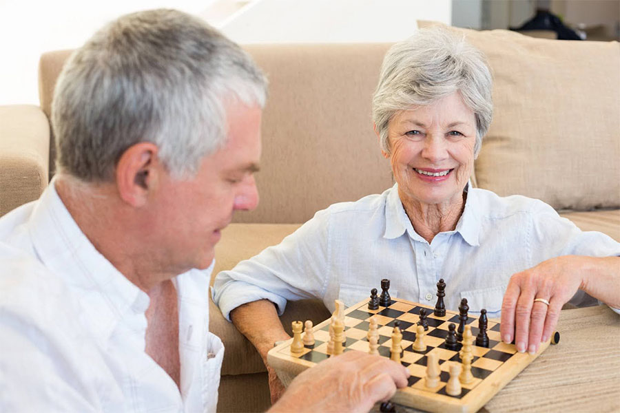 Older man and woman playing chess together, showing supportive activities for people living with dementia.