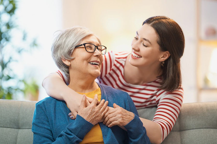 Younger woman smiling with her mother, offering support and care for a loved one with early-onset dementia. Younger woman smiling with her mother, offering support and care for a loved one with early-onset dementia.