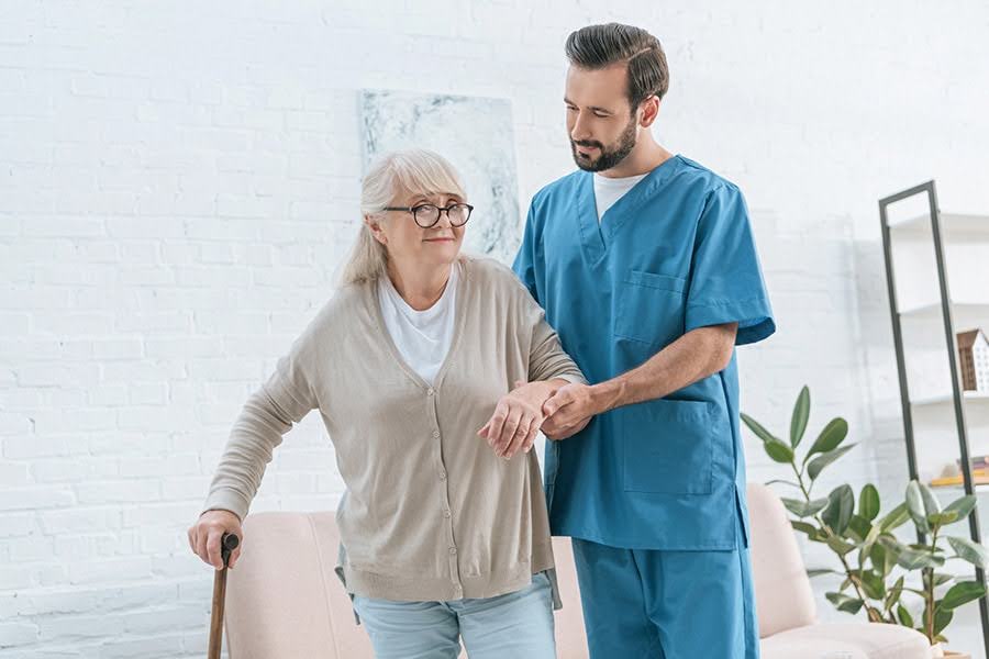 A caregiver helping an elderly woman stand with a cane, representing the challenges of caregiver burnout