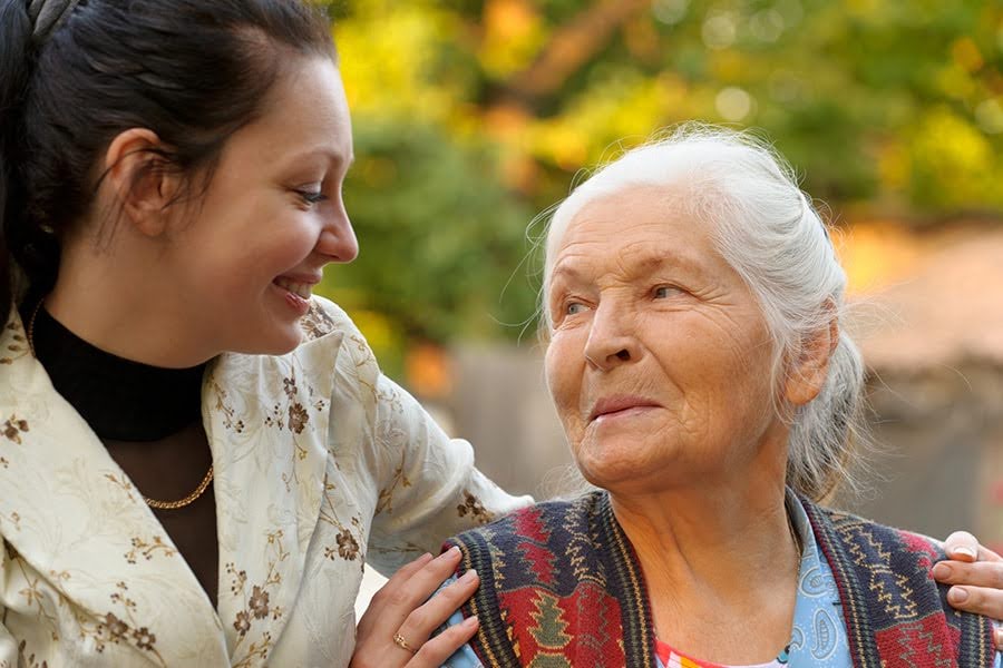 A caregiver smiling at an elderly woman outdoors, representing compassionate respite care in Maryland