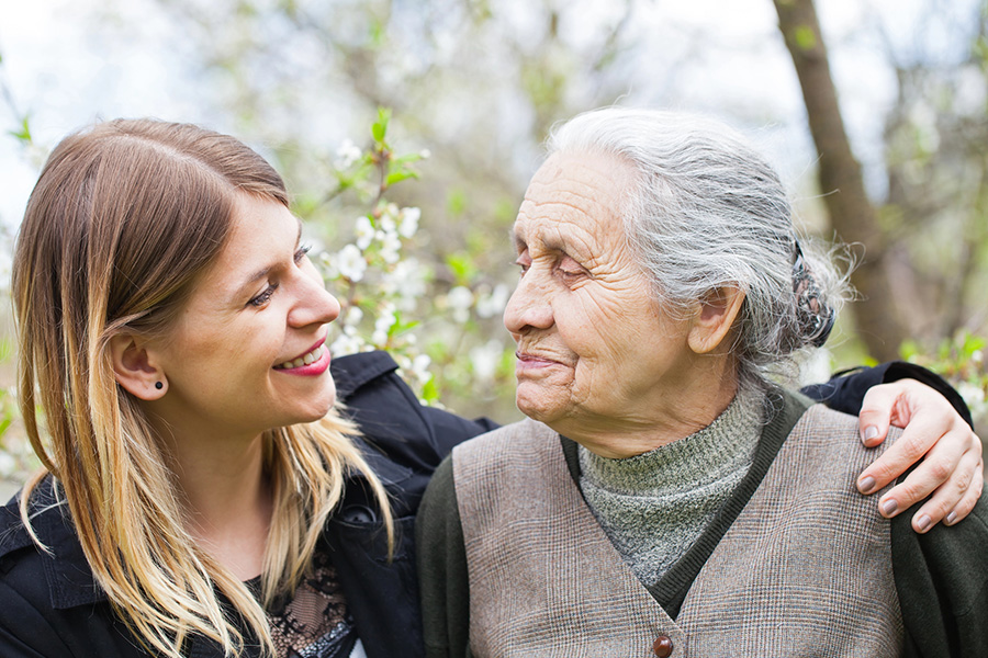 Young woman smiling and embracing an older woman outdoors, illustrating support for someone with late stage dementia Young woman smiling and embracing an older woman outdoors, illustrating support for someone with late stage dementia