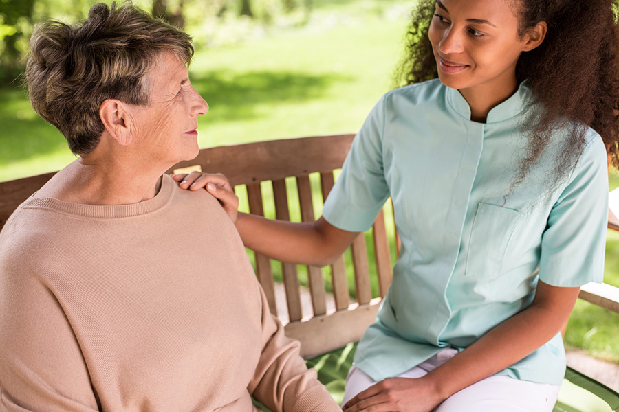 Caregiver gently supporting an older woman on a park bench, illustrating mild cognitive impairment during daily care.