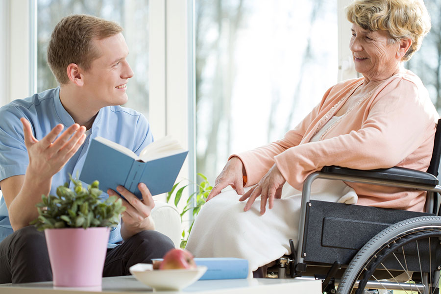 Caregiver reading with an older woman in a wheelchair supporting routines related to what stage of dementia is sundowning