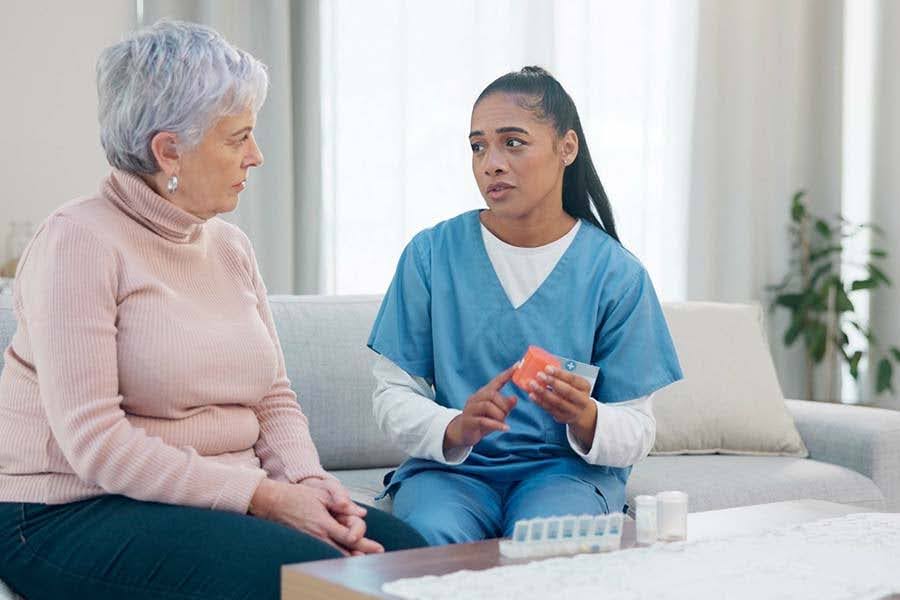 A caregiver in scrubs discusses prescription medications with a senior woman