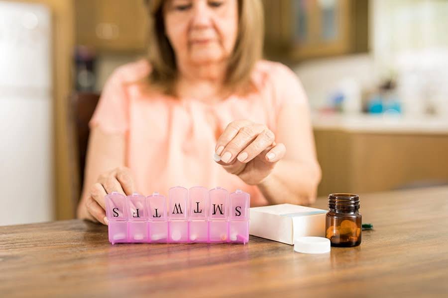 A senior woman uses a pill organizer for medication management for seniors in a home setting A senior woman uses a pill organizer for medication management for seniors in a home setting