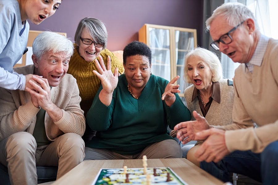 social activities for seniors playing a board game together in a group, laughing and reacting at a table social activities for seniors playing a board game together in a group, laughing and reacting at a table