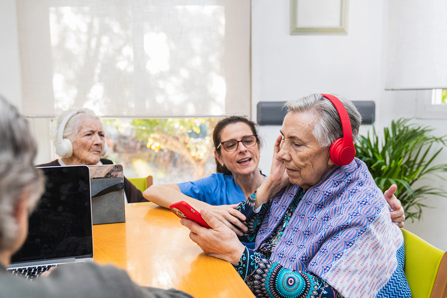 Senior women enjoying engaging memory care activities, like listening to music with headphones and using a smartphone.