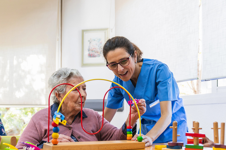 A caregiver assists a senior with a bead maze, showcasing memory care activities near Montgomery Village, MD.