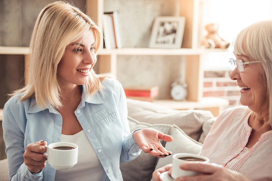 A smiling woman and senior enjoy coffee together, highlighting the importance of caregiver self-care and connection.