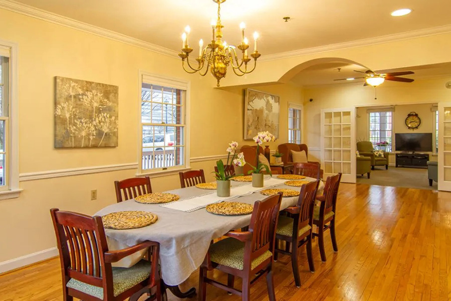 Bright, open dining area at Auxiliary House featuring a set wooden table, warm lighting, and a homelike atmosphere.