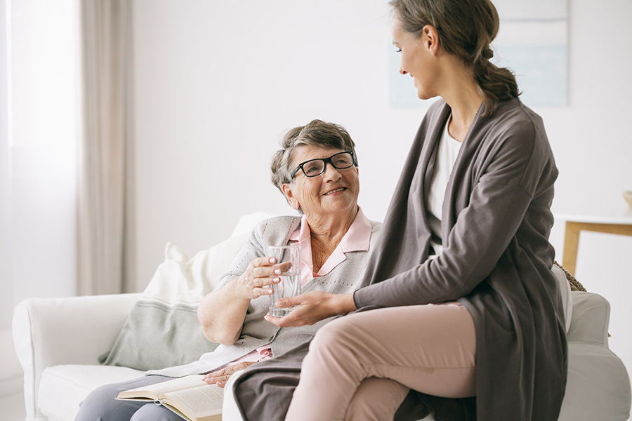 Caregiver assisting an elderly woman at home while discussing the difference between memory care and assisted living.